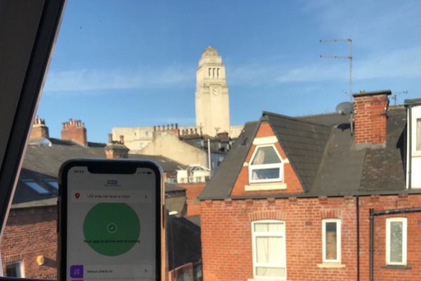 Phone showing NHS Test and Trace app, held up with view of Parkinson Building in the background.