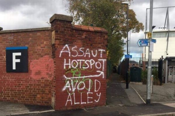 Wall with graffiti saying "assault hotspot, avoid alley"